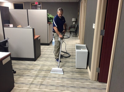 A Duo Care worker operating a carpet cleaning wand in an office