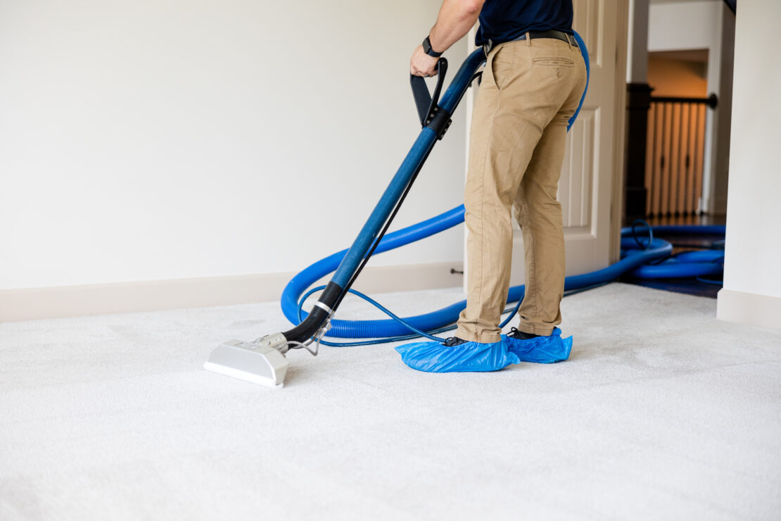 A person wearing booties steam cleans white carpet