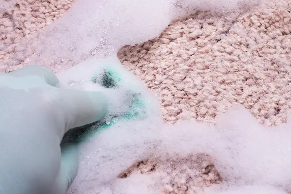 Cleaning carpet by a detergent with a lot of foam. Hand in green rubber glove washing carpet by a green sponge. Spring cleaning in house